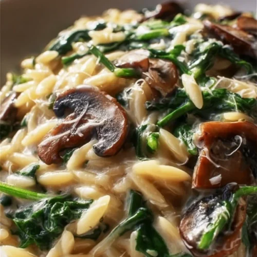 Creamy orzo dish with mushrooms and fresh spinach served in a bowl